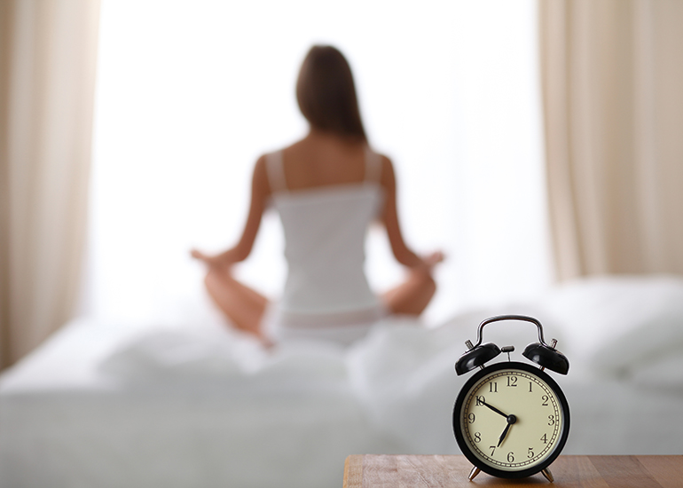 Woman sitting on bed meditating in early morning